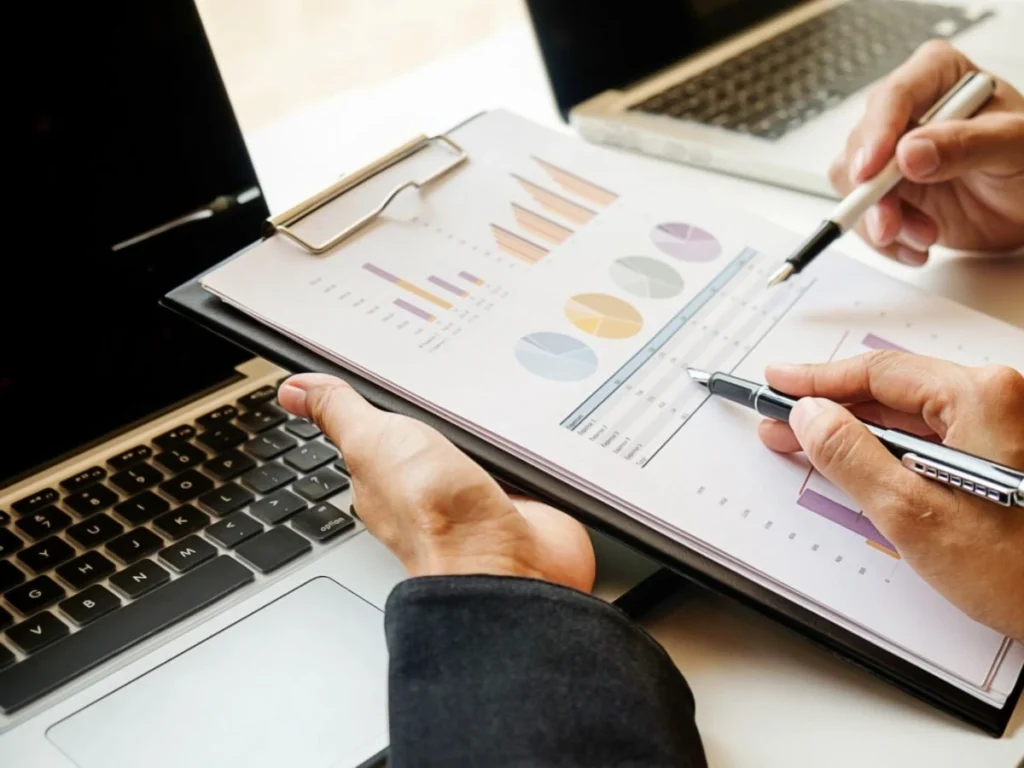 Marketing digital Dos analistas revisando gráficos de rendimiento y métricas impresas sobre portátiles, representando el servicio de análisis y reportes de Domina Internet en Barcelona.